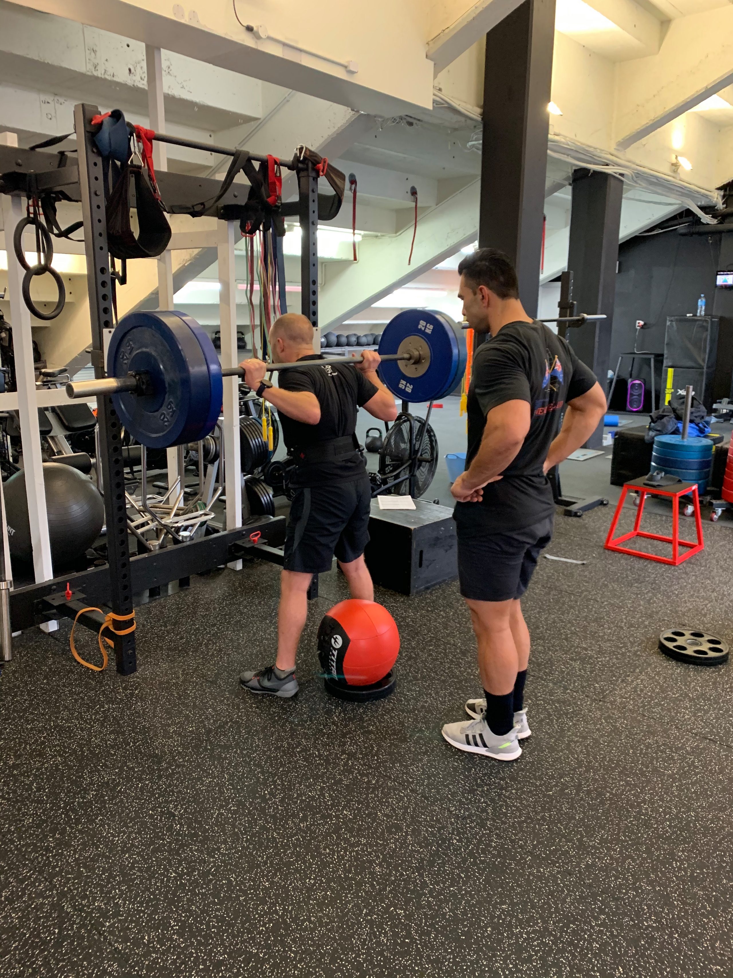 Middle-aged man lifting weights with personal trainer support at Body Torque Gym in Newmarket, Auckland.