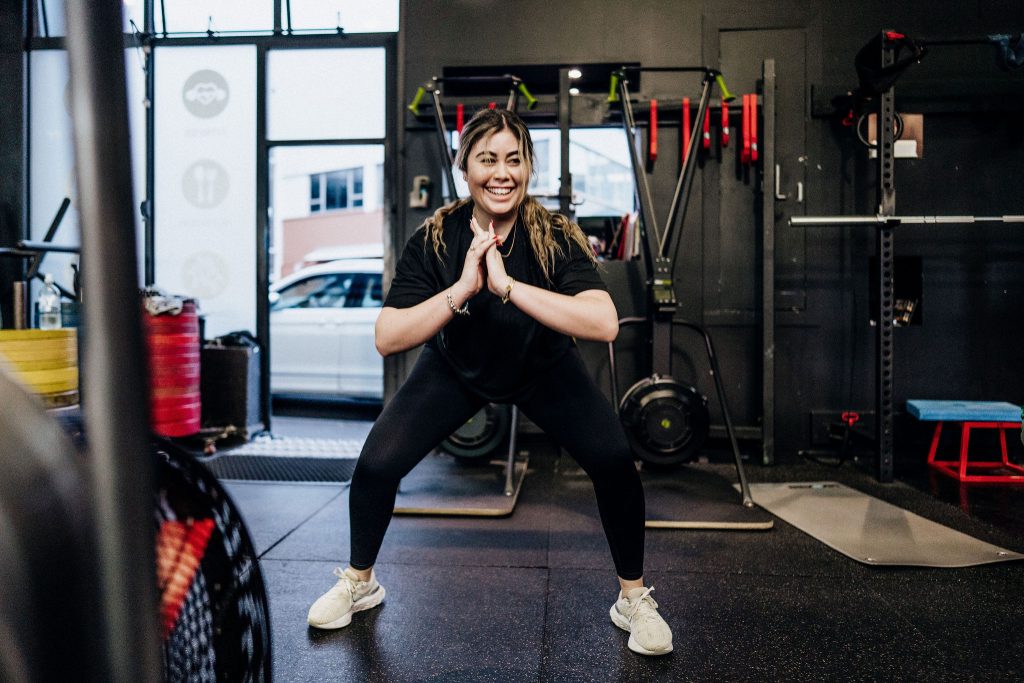 Smiling woman performing a squat exercise during a training session at Body Torque Gym in Newmarket, Auckland.