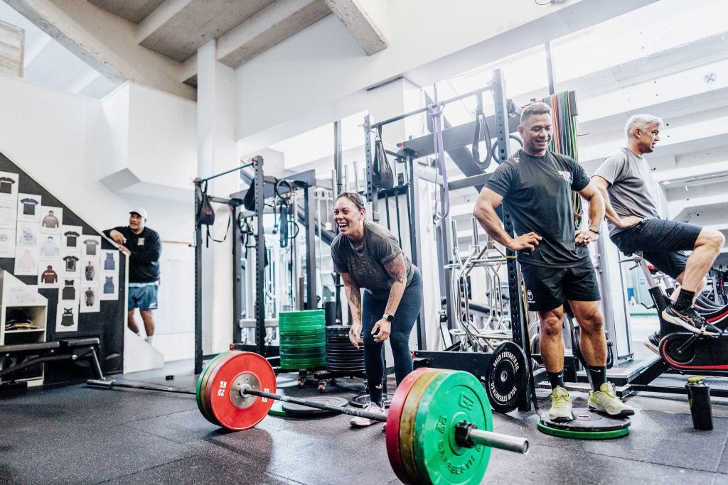 Body Torque Gym members smiling and lifting weights during a strength training session in Newmarket, Auckland.