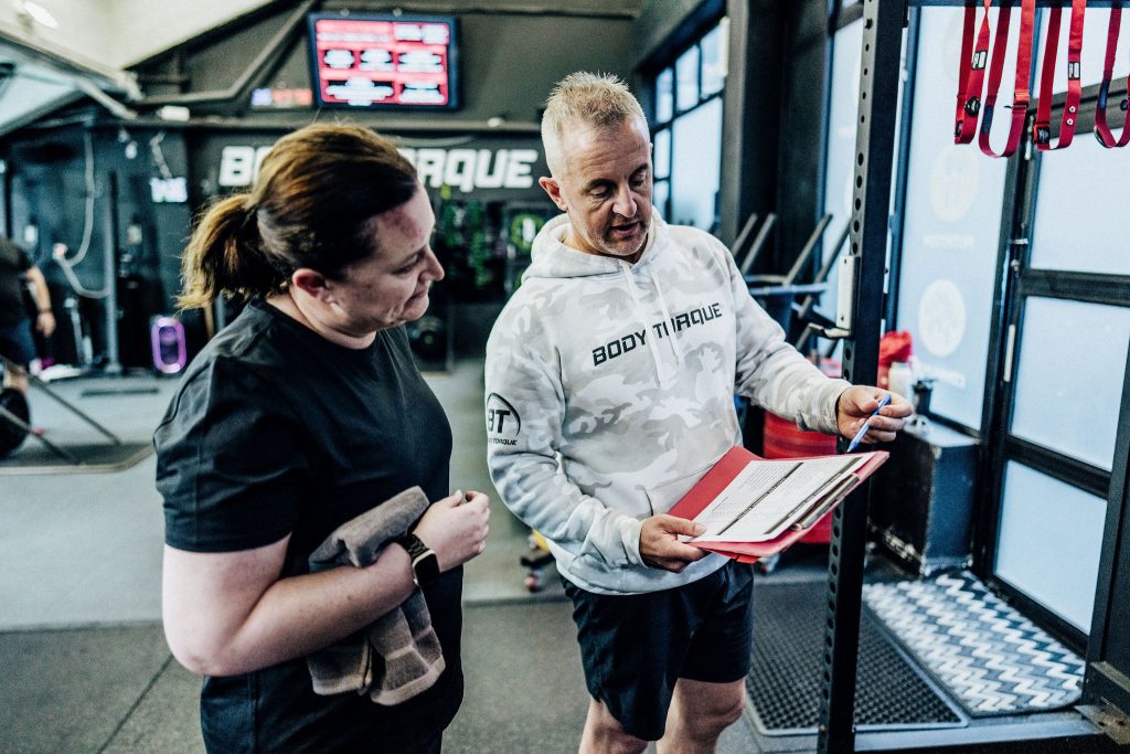 Alex Flint, personal trainer at Body Torque Gym, discussing a customised training plan with a female client in Newmarket, Auckland.