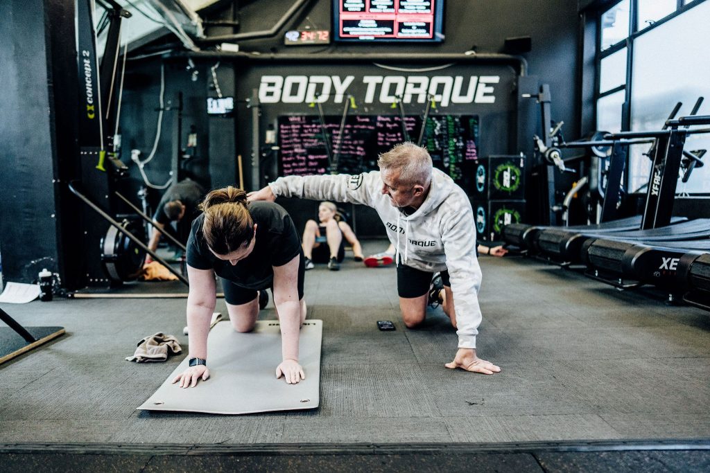 Alex Flint, personal trainer at Body Torque Gym in Newmarket, Auckland, correcting a client's exercise technique for safe and effective training.