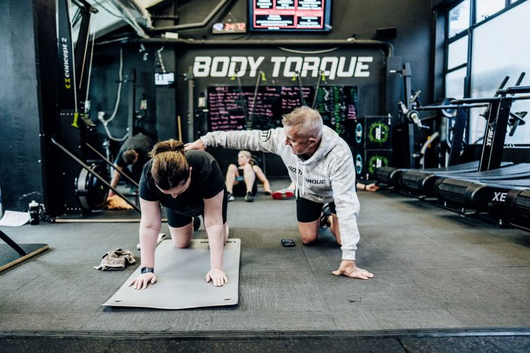 Alex Flint, personal trainer at Body Torque Gym in Newmarket, Auckland, correcting a client's exercise technique for safe and effective training.