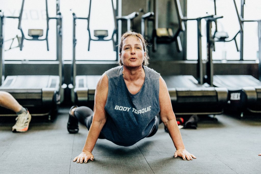 Middle-aged woman in a Body Torque Gym T-shirt performing a floor stretch exercise at Body Torque Gym in Newmarket, Auckland.