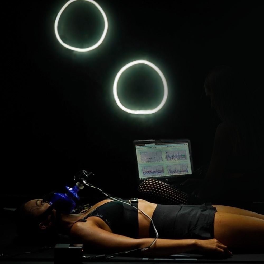 Middle-aged woman lying down wearing a metabolic testing mask connected to a computer analysing results.