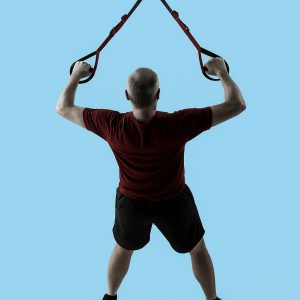 Middle-aged man in activewear performing Alex Flint suspension trainer exercise against a light blue background.